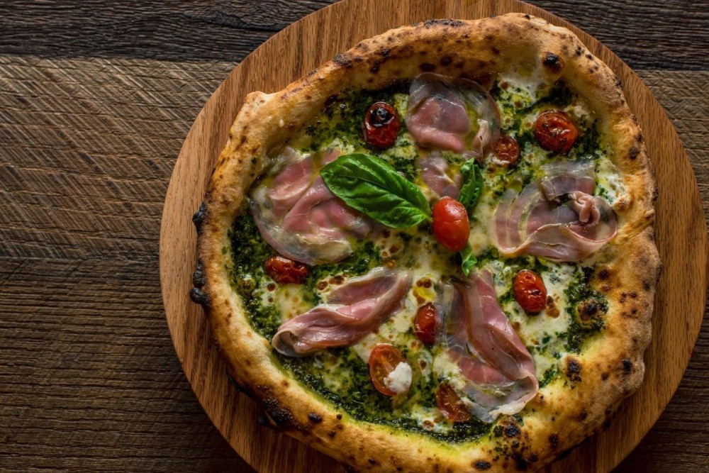 pizza on a plate with basil, prosciutto and cherry tomatoes